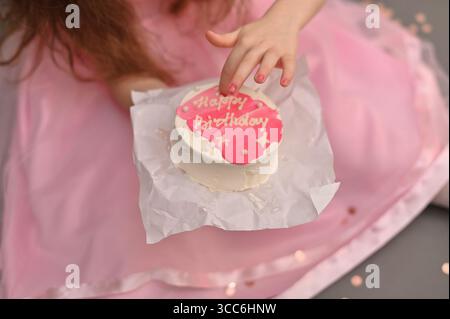 Primo piano di biscotti rosa a mano con buon compleanno scritto in glassa. la ragazza tiene in mano una torta decorata, sottolineando il tema del compleanno e. Foto Stock