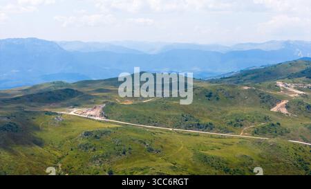Vista panoramica dell'altopiano di Jahorina con strade tortuose e colline erbose aperte sotto il cielo morbido Foto Stock
