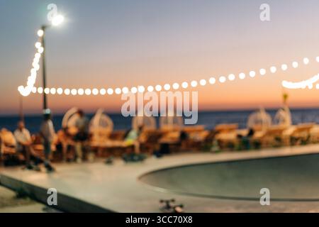 Sfondo sfocato e sfocato di uno skate Park con garland sulla spiaggia al tramonto con spazio per copiare. Foto Stock