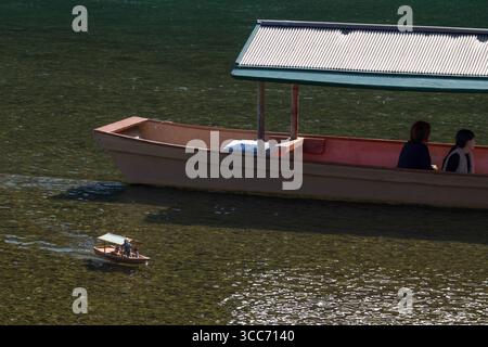 Due persone si godranno un tranquillo giro in barca sulle acque calme con una barca in miniatura in primo piano, creando una scena pacifica e riflettente. Fiume Katsura, U Foto Stock