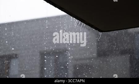 Forte pioggia che cade dal bordo del tetto con corsi d'acqua Foto Stock