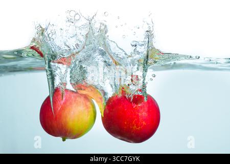 Spruzzi dinamici di due mele rosse che colpiscono la superficie dell'acqua, creando bolle e increspature in un ambiente di acqua limpida. Foto Stock