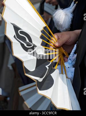 Un uomo giapponese che tiene in mano una carta pieghevole "sensu" (扇子) e un ventilatore di bambù con un design bianco e nero in un evento in Giappone. Foto Stock