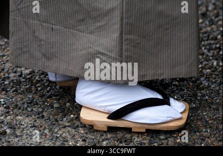 Un uomo giapponese in kimono che indossa i tradizionali sandali geta di legno (下駄) con calzini bianchi "tabi" (旅) a punta divisa che sono ancora di moda in Giappone. Foto Stock