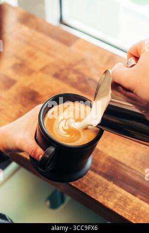 Il barista versa latte Art nella tazza nera Foto Stock
