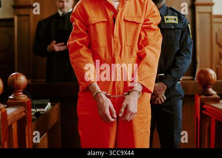Giovane uomo caucasico adulto in manette in piedi in tribunale durante il processo Foto Stock
