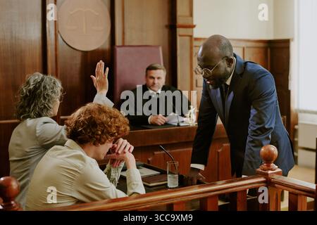 Black Man di mezza età che si rivolge a clienti caucasici durante il processo giudiziario Foto Stock