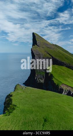 Le torreggianti scogliere di Mylingur si innalzano drammaticamente dalla costa delle Isole Faroe, circondate da una vegetazione lussureggiante e da un vasto oceano. Foto Stock