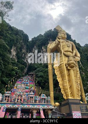 L'imponente statua dorata di Lord Murugan e le colorate scale alle grotte di Batu, in Malesia, con scogliere calcaree sullo sfondo. Foto Stock