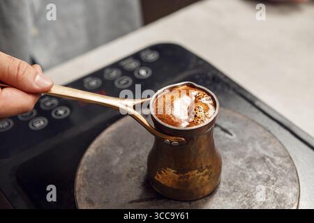 Preparazione tradizionale di caffè turco in un Dzezva su piano cottura con cucchiaio Foto Stock