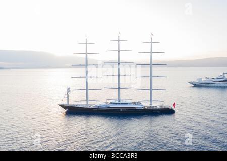 Idra, Grecia - 30 luglio 2025: Veduta aerea di un maestoso yacht a vela che attraversa le tranquille acque baciate dal sole, una danza dello scafo scuro contro il mare scintillante. Foto Stock