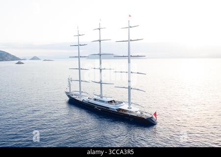 Idra, Grecia - 30 luglio 2025: Vista aerea di un maestoso yacht a vela che scivola sulle acque tranquille, i suoi torreggianti alberi che raggiungono il cielo pallido. Foto Stock