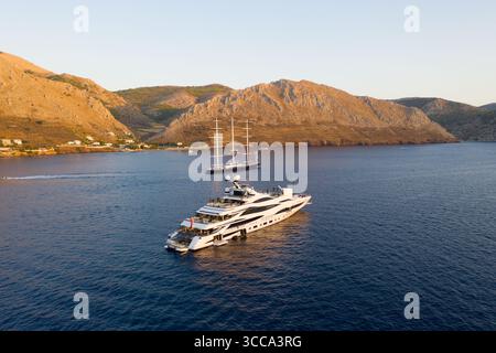 Idra, Grecia - 30 luglio 2025: Veduta aerea di lussuosi yacht che riposano sul mare blu profondo, incorniciati da aspre colline sotto un cielo caldo ed esteso. Foto Stock