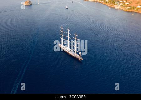 Idra, Grecia - 30 luglio 2025: Veduta aerea di una maestosa nave a quattro alberi che naviga sul mare blu profondo, le vele bianche contrastano con l'acqua scura e la costa lontana. Foto Stock