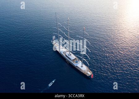 Idra, Grecia - 30 luglio 2025: Veduta aerea di un maestoso e moderno yacht a vela che attraversa il blu intenso dell'Egeo, i suoi torreggianti alberi e lo scafo elegante a testimonianza del lusso e dell'avventura. Foto Stock