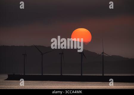 Turbine eoliche che generano energia rinnovabile durante un vibrante tramonto nel porto di bilbao, biscaglia, spagna, che mostra la transizione verso l'energia sostenibile Foto Stock