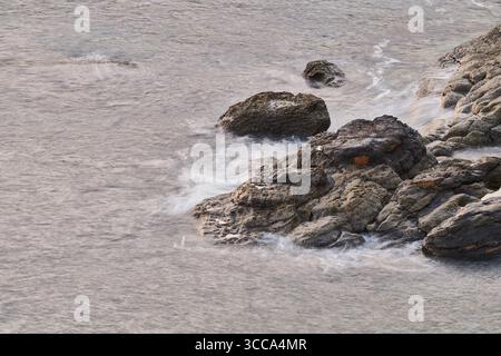 Onde dolci che scivolano sulle rocce sulla costa di castro urdiales, cantabria, spagna, creando una tranquilla scena di bellezza della natura Foto Stock