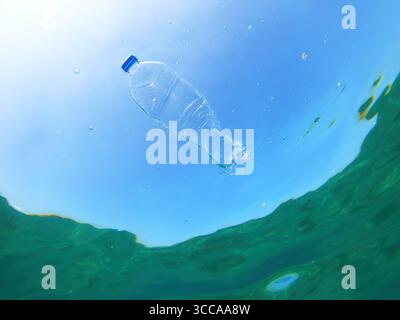 Una bottiglia di plastica scartata galleggia nelle acque cristalline dell'oceano, simboleggiando l'inquinamento marino e il problema globale dei rifiuti di plastica negli ambienti naturali.bassa Foto Stock