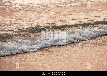 Dolce onda di mare con schiuma bianca che rotola sulla spiaggia di sabbia al tramonto a Halkidiki, Grecia. Messa a fuoco selettiva. Foto Stock