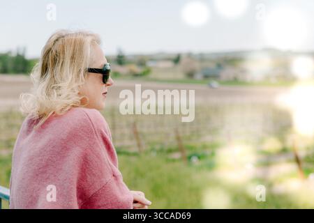 Una donna con maglione rosa guarda il vigneto sotto la luce soffusa del sole Foto Stock