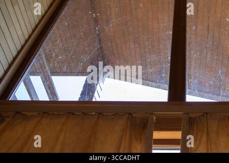 Grande finestra triangolare coperta da ragnatele e sporcizia all'interno di case in legno era necessaria una pulizia rustica degli interni Foto Stock