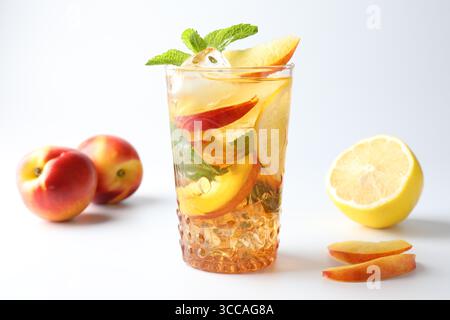 Gustoso tè freddo con limone, pesche e menta su sfondo bianco Foto Stock