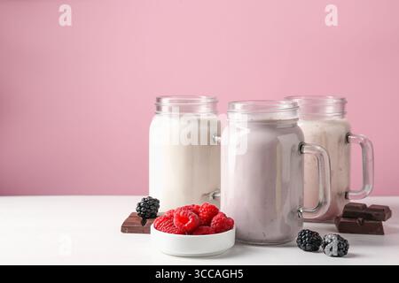 Diversi frullati gustosi nei vasetti mason e ingredienti su un tavolo bianco, spazio per il testo Foto Stock