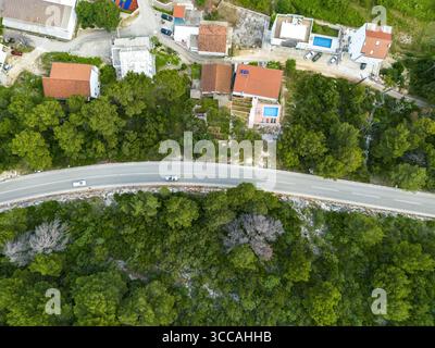 Vista aerea della strada serpentina che si snoda attraverso una vegetazione lussureggiante, in contrasto con i tetti di tegole rosse delle case costiere annidate tra gli alberi, Drvenik, Spalato-Dalmazia County, Croazia. Foto Stock