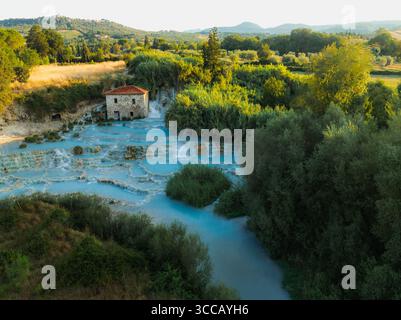 Veduta aerea delle cascate e delle acque azzurre delle sorgenti termali in contrasto con la vegetazione verdeggiante e un edificio in pietra, Saturnia, Toscana Foto Stock