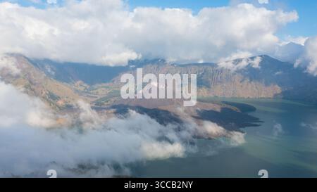 Vista aerea del maestoso Monte Rinjani che attraversa un mare di nuvole eteree, cullato dalle tranquille acque del Lago Segara Anak, Lombok, West Nusa Tenggara, Indonesia. Foto Stock