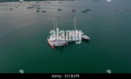 Vista aerea di catamarani e yacht ormeggiati in calme acque turchesi, una tranquilla scena portuale sotto un cielo morbido, Bali, Indonesia. Foto Stock