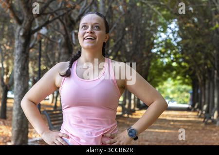 Ritratto di una donna sorridente dopo aver corso. Una donna sana si riposa dopo l'allenamento e guarda nella fotocamera. Donna sportiva e attiva che ama l'aria aperta Foto Stock