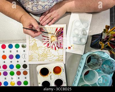 Vista dall'alto della donna che dipinge con cura intricati motivi floreali di Batik utilizzando colori vivaci in uno spazio di lavoro creativo. kuala lumpur, malesia Foto Stock