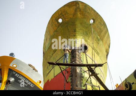 Dhaka, Bangladesh - 29 dicembre 2020: Vista di un lavoratore precariamente equilibrato su impalcature, oscurato dal colossale scafo intempestivo di una nave in riparazione, colori. Foto Stock