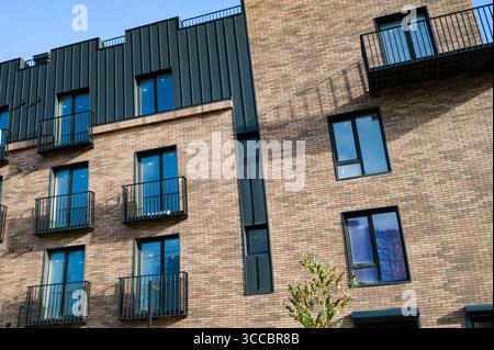 Un edificio contemporaneo presenta una combinazione di eleganti rivestimenti in metallo e mattoni caldi, con balconi che gettano interessanti ombre in una giornata limpida Foto Stock