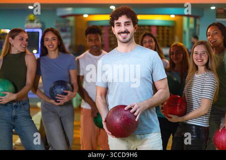 Giovani adulti con palle da bowling, sorridono e si divertono una serata di bowling con gli amici Foto Stock
