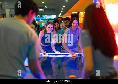 Gruppo di amici che si divertono a giocare a hockey da tavolo in una vivace sala giochi con luci colorate Foto Stock