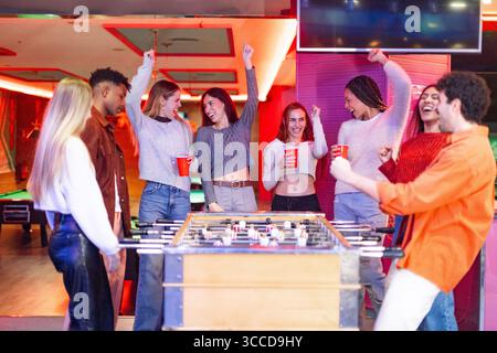 Gruppo di allegri amici multietnici che si divertono giocando a calcio e bevendo in un pub Foto Stock