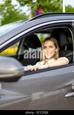 Giovane donna d'affari sorridente mentre guida la sua auto moderna, godendosi la guida e sentendosi sicura di sé Foto Stock