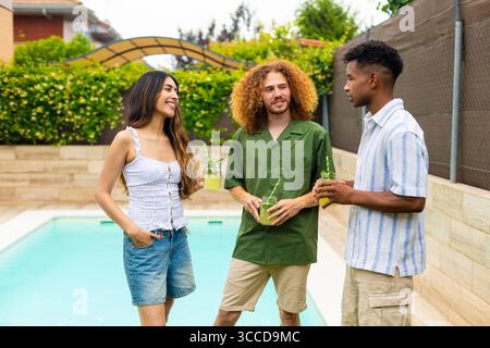 Tre amici stanno socializzando e gustando rinfrescanti cocktail mojito in piscina durante un incontro estivo Foto Stock