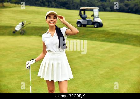 Una golfista sicura di sé è pronta sul green, anticipando una partita emozionante, con un elegante golf cart sullo sfondo, che incarna il tempo libero e. Foto Stock