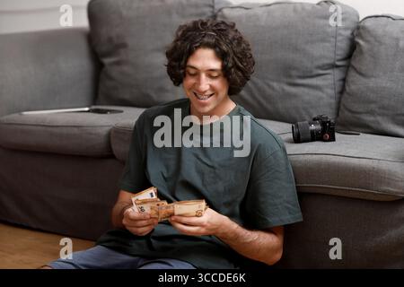 Giovane felice che conta i soldi guadagnati con il suo lavoro di fotografo o videografo Foto Stock