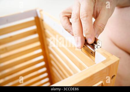 Primo piano della mano del falegname che installa una cerniera in metallo su una struttura in legno, dimostrando precisione e maestria artigianale Foto Stock