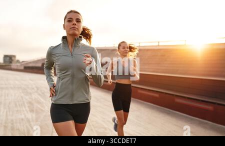 Due donne entusiaste si impegnano energicamente in una corsa vivace su una pista da corsa durante un bellissimo tramonto, trasudando motivazione ed energia contagiosa, Foto Stock