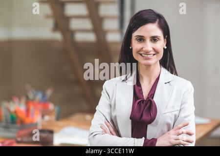 scrivania in legno con penne e carte colorate in ufficio mentre la scala si appoggia contro la parete beige. Professional, Workspace, Contemporary, creative, corpor Foto Stock