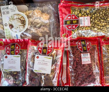 Primo piano di varie confezioni di erbe e frutta essiccate medicinali cinesi in mostra confezioni rosse vibranti e testo ed etichette cinesi nella sala medica di singapore Foto Stock