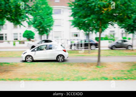 Un'immagine vibrante che cattura una berlina bianca in movimento dinamico, simboleggia la natura frenetica della vita cittadina e gli spostamenti quotidiani. Foto Stock