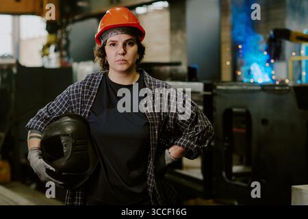 Ritratto di una giovane donna caucasica adulta che indossa un cappello duro in piedi in officina Foto Stock