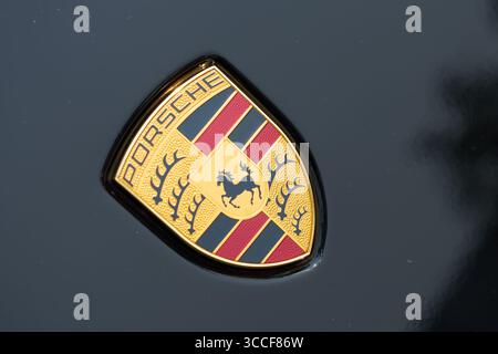 Primo piano del logo Porsche dorato con dettagli rossi e neri su una superficie nera lucida. Foto Stock