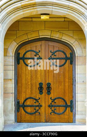 Le porte ornate in legno con cerniere in ferro battuto sorgono sotto un arco di pietra al Trinity College Foto Stock